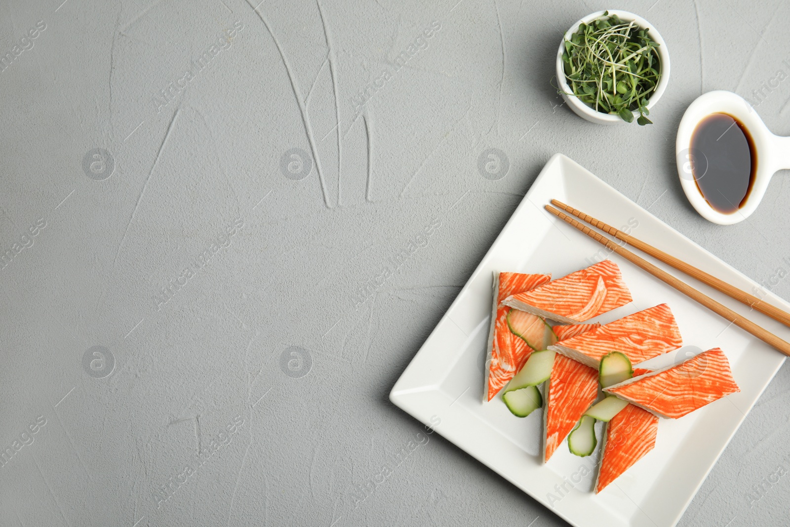 Photo of Fresh crab sticks with cucumber served on grey table, flat lay. Space for text