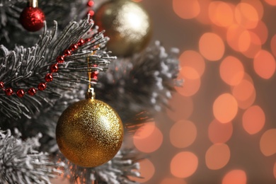 Photo of Golden holiday bauble hanging on Christmas tree against blurred festive lights, closeup. Space for text