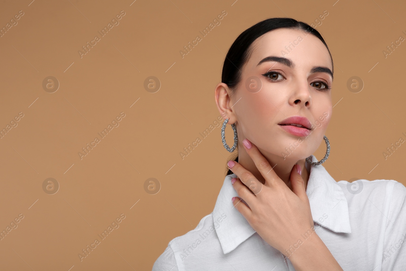 Photo of Beautiful young woman with elegant earrings on beige background. Space for text