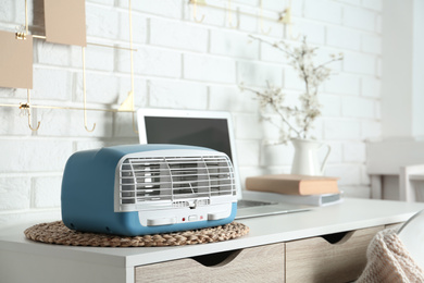 Photo of Modern air purifier near laptop on white wooden table in room