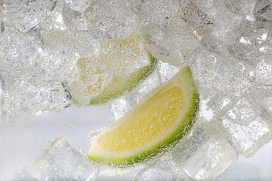 Photo of Juicy lime slices and ice cubes in soda water against white background, closeup