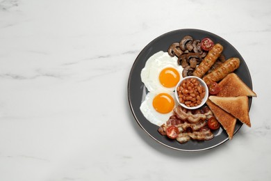 Photo of Plate of fried eggs, mushrooms, beans, tomatoes, bacon, sausages and toasts on white marble table, top view. Traditional English breakfast