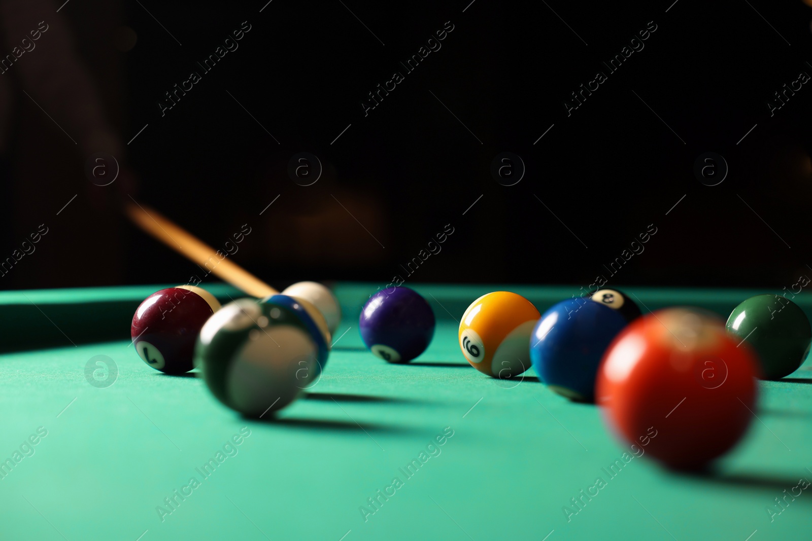 Photo of Many colorful billiard balls and cue on green table indoors