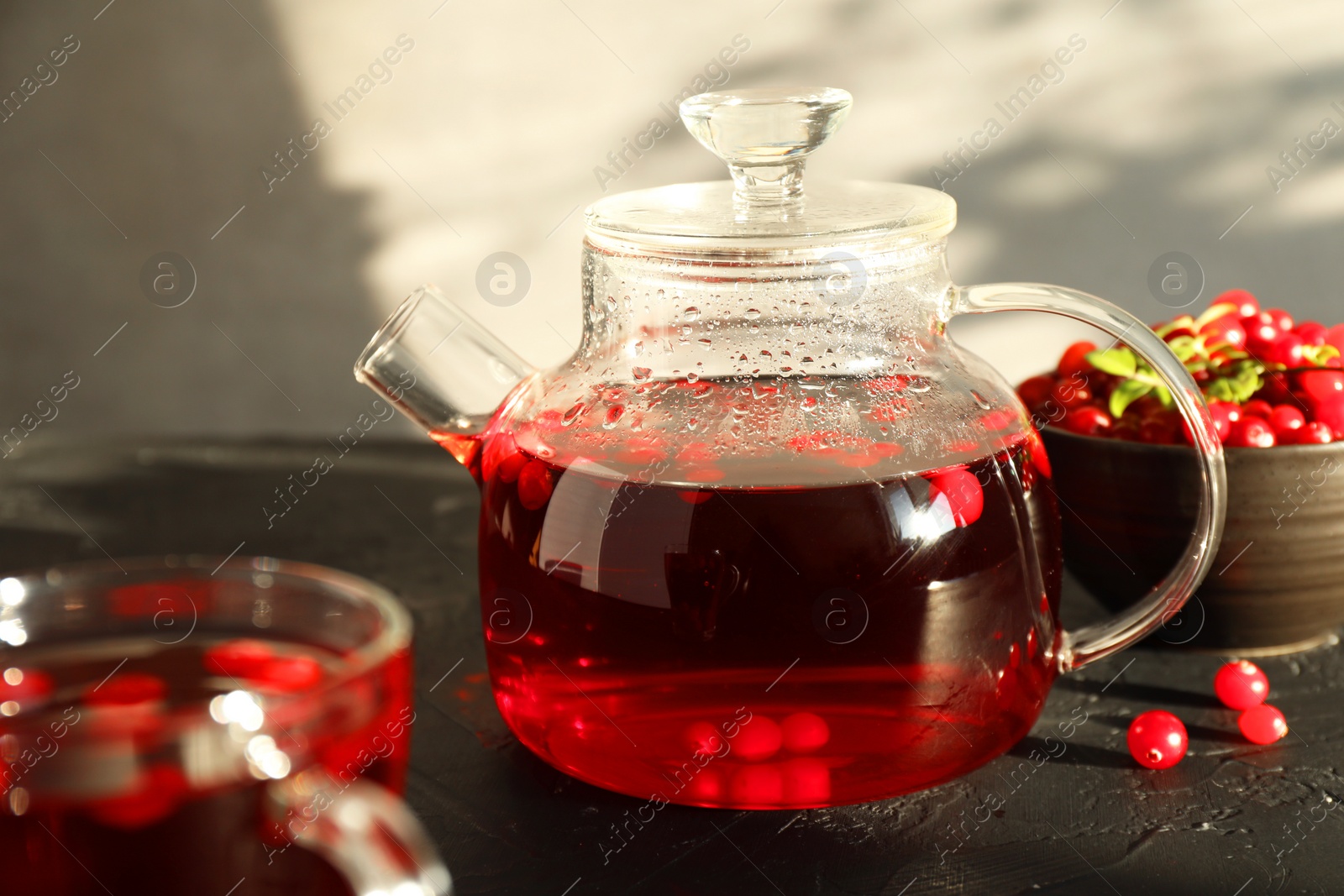 Photo of Tasty hot cranberry tea in teapot and fresh berries on black textured table