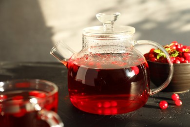 Tasty hot cranberry tea in teapot and fresh berries on black textured table