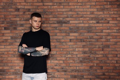 Young man with tattoos near brick wall. Space for text