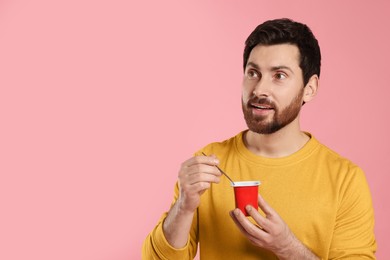 Photo of Handsome man with delicious yogurt and spoon on pink background. Space for text