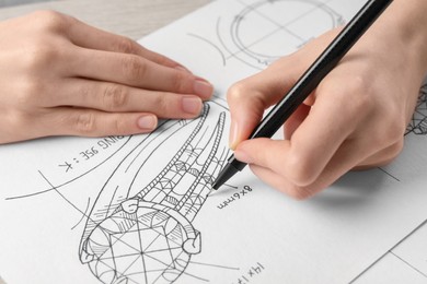 Photo of Jeweler drawing sketch of elegant ring on paper at wooden table, closeup