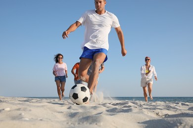 Photo of Group of friends playing football at beach, focus on ball