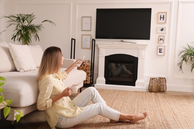 Photo of Young woman watching television at home. Living room interior with TV on fireplace