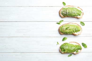 Photo of Tasty avocado sandwiches on white wooden table, flat lay. Space for text