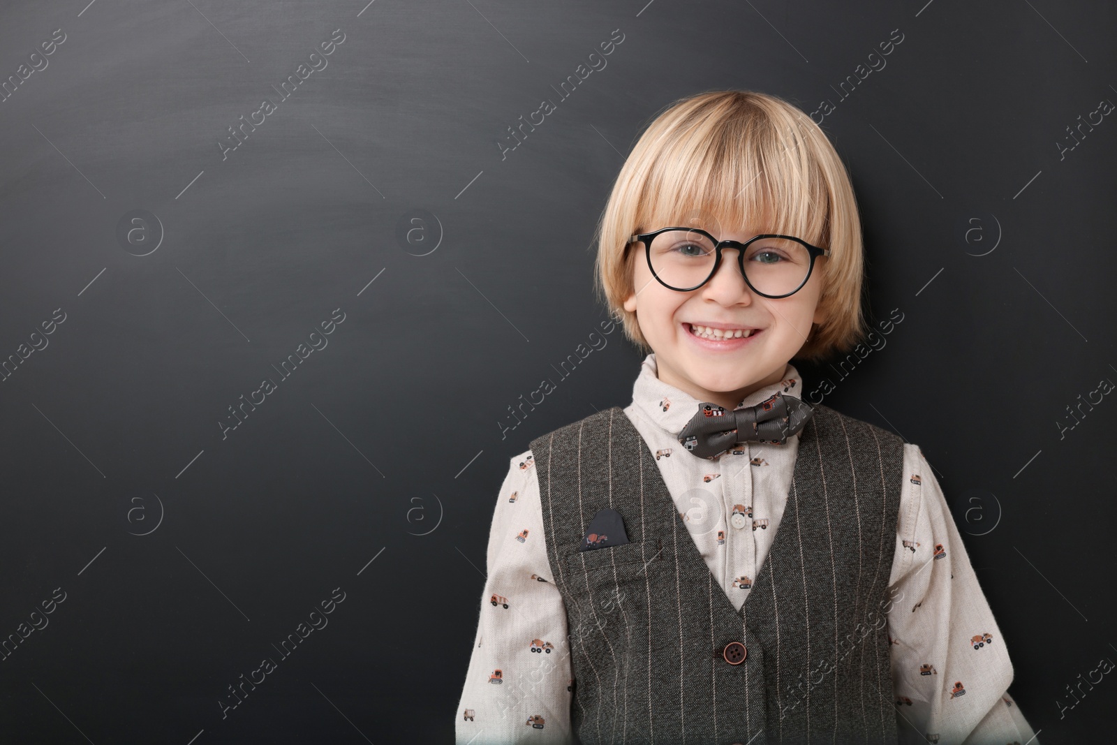 Photo of Happy little school child in uniform near chalkboard. Space for text