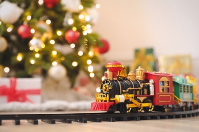 Photo of Toy train and railway near Christmas tree indoors. Space for text