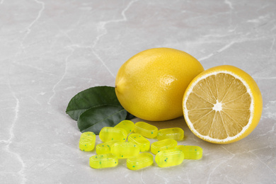 Photo of Tasty candy drops and fresh lemon on grey marble table