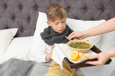 Young woman bringing broth to her sick son in bed. Cold treatment