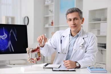 Gastroenterologist showing anatomical model of large intestine at table in clinic