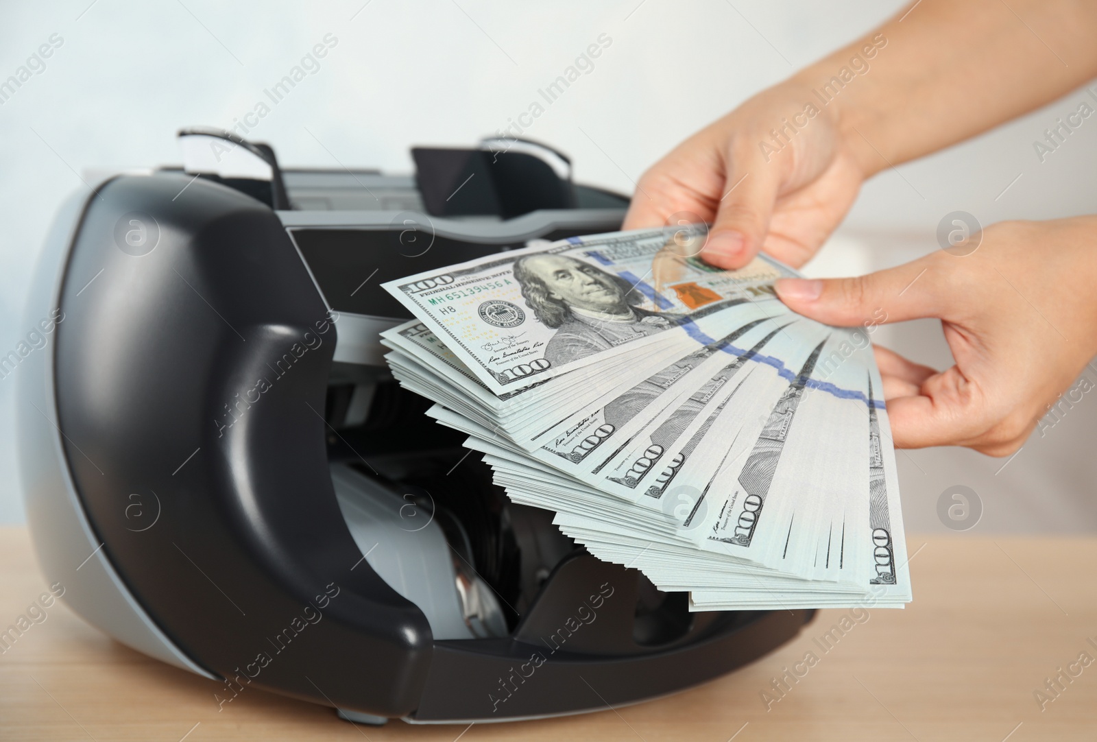 Photo of Woman holding money near counting machine at table indoors, closeup