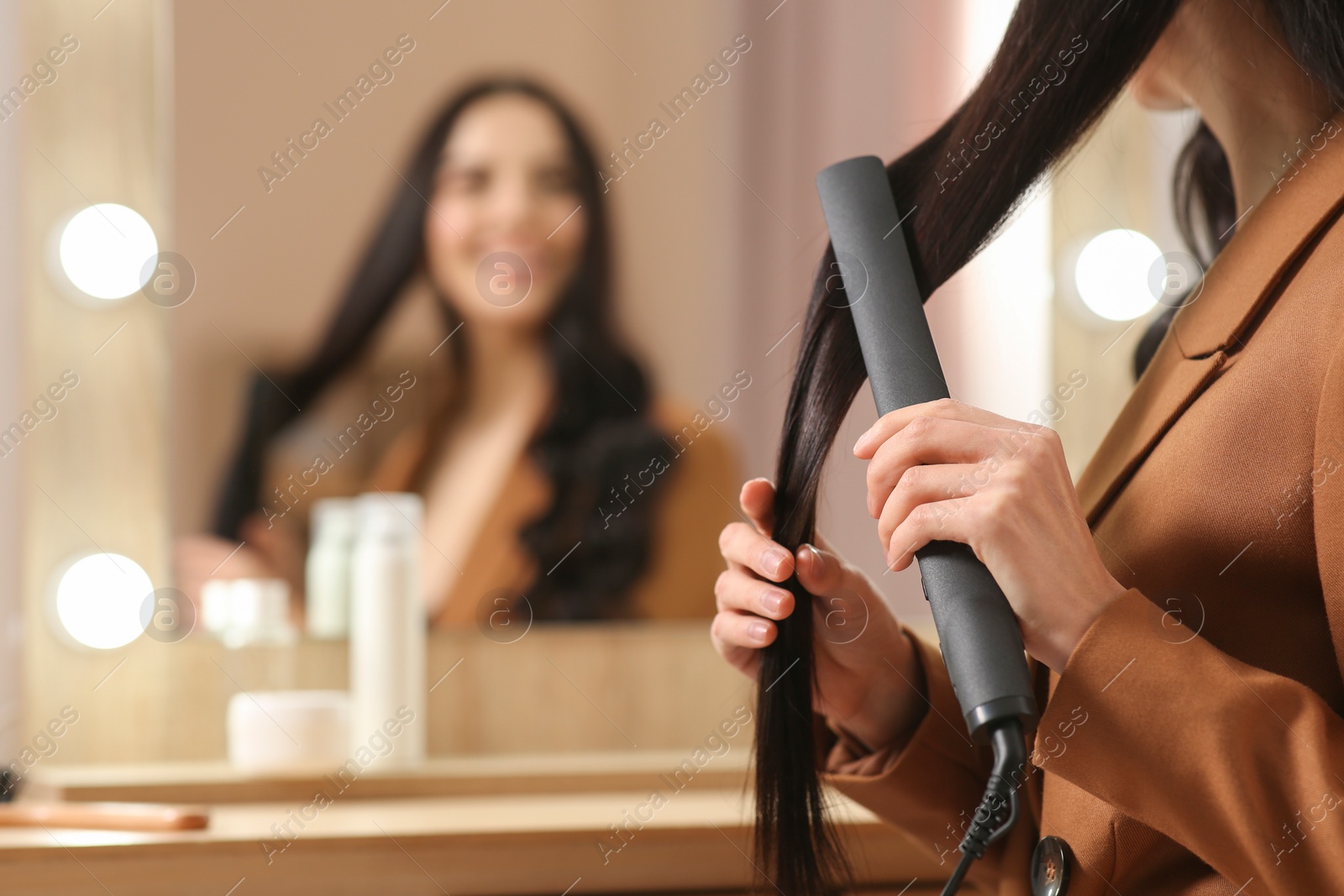 Photo of Woman using hair iron near mirror indoors, closeup. Space for text