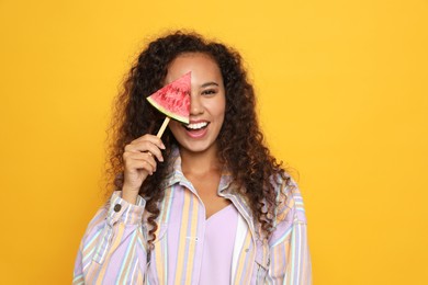 Beautiful young African American woman with piece of watermelon on yellow background