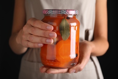 Photo of Woman holding jar with pickled carrot against black background, closeup