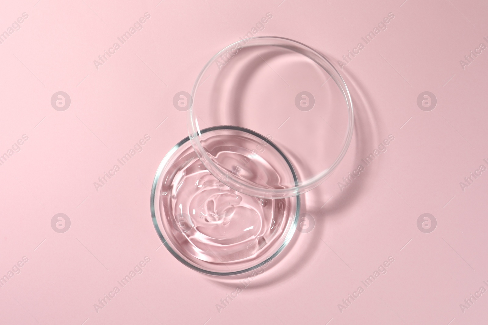 Photo of Petri dish with liquid and lid on pale pink background, flat lay