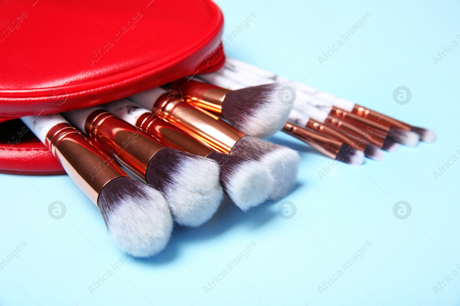 Photo of Bag with professional makeup brushes on light blue background