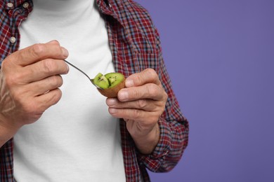 Photo of Man eating kiwi with spoon on purple background, closeup. Space for text