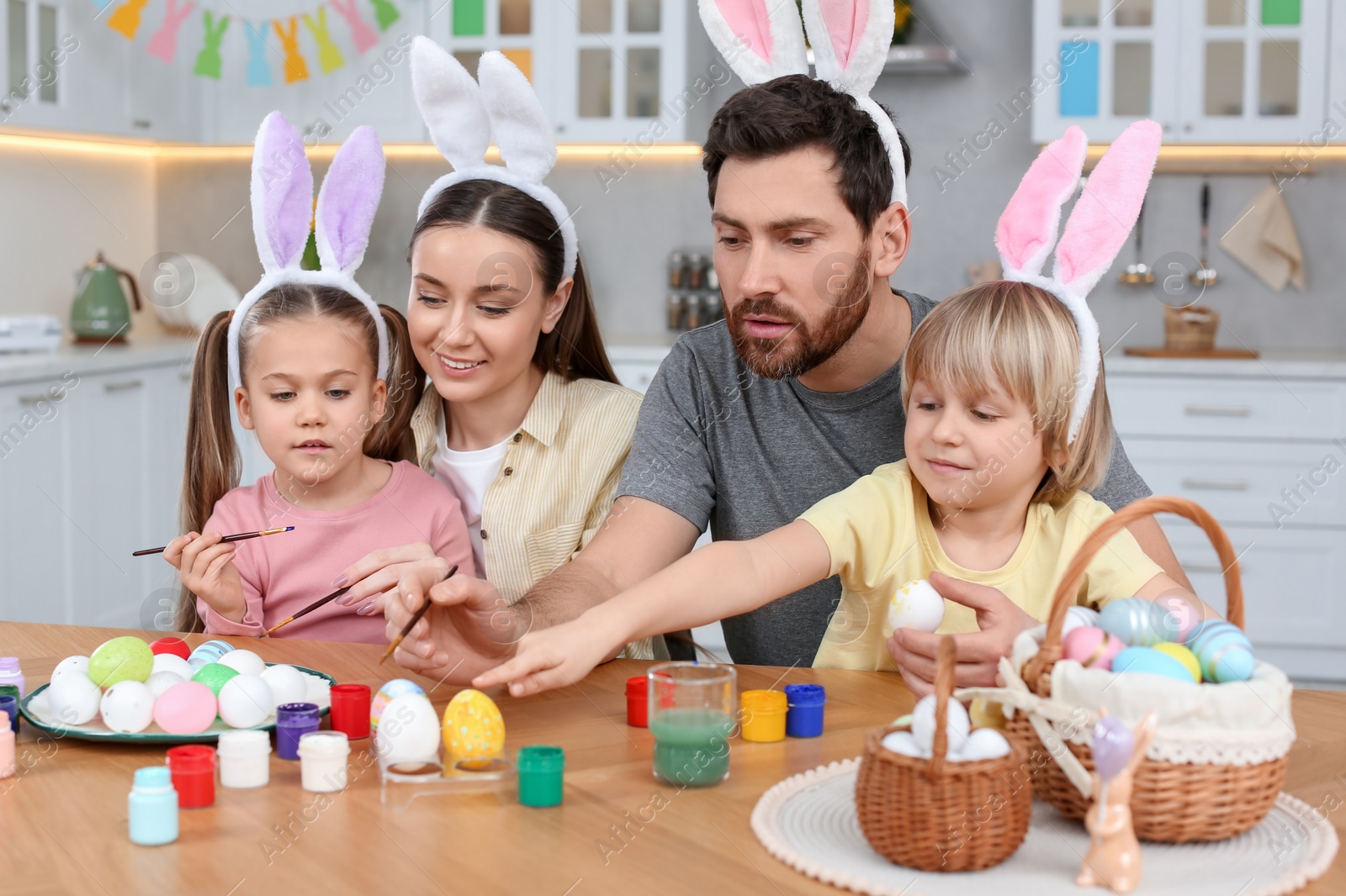 Photo of Happy family painting Easter eggs at table in kitchen