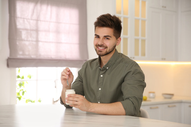 Photo of Happy young man with tasty yogurt at table in kitchen