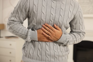 Photo of Young man suffering from stomach pain indoors, closeup