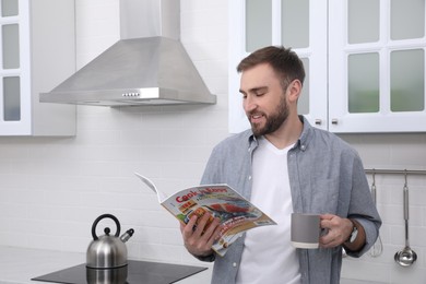 Handsome man with cup of coffee reading magazine in kitchen