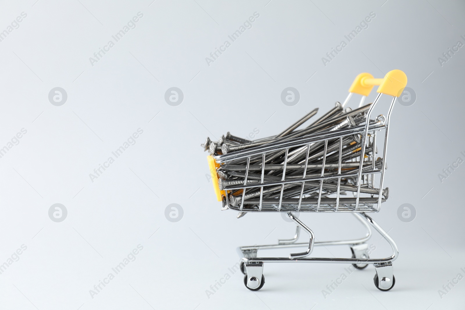 Photo of Metal nails in shopping cart on light grey background, space for text