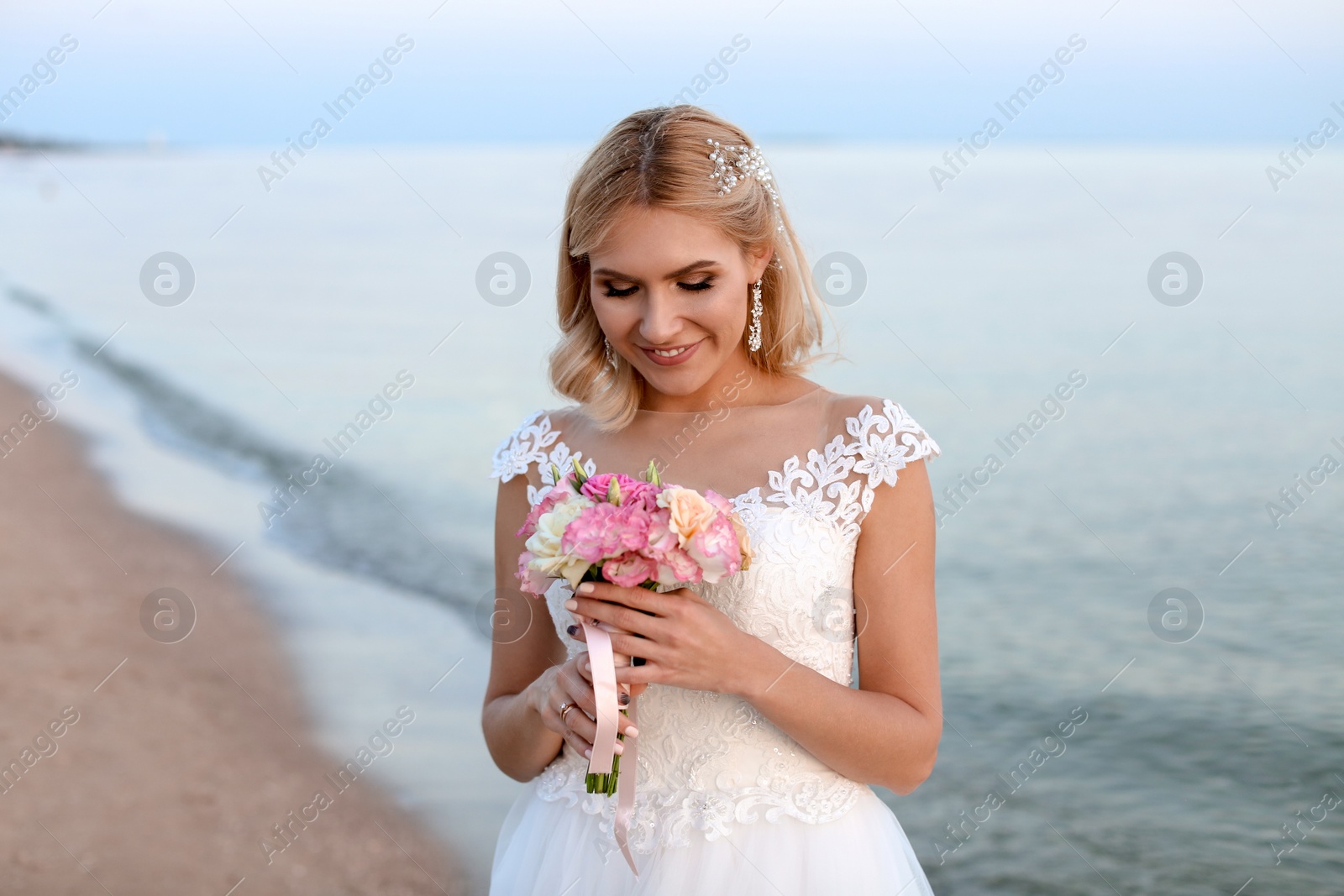 Photo of Happy bride holding wedding bouquet on beach