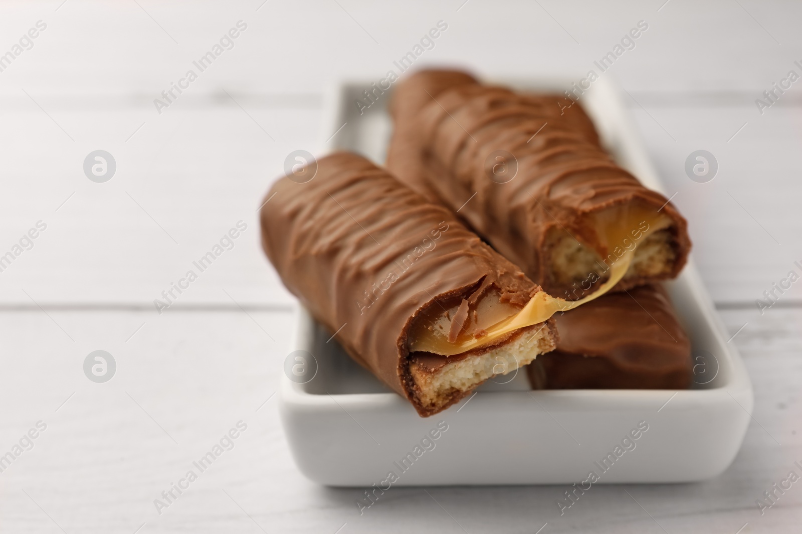 Photo of Tasty chocolate bars with caramel on white wooden table, closeup. Space for text