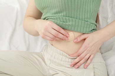 Photo of Woman applying contraceptive patch onto her belly on bed, closeup