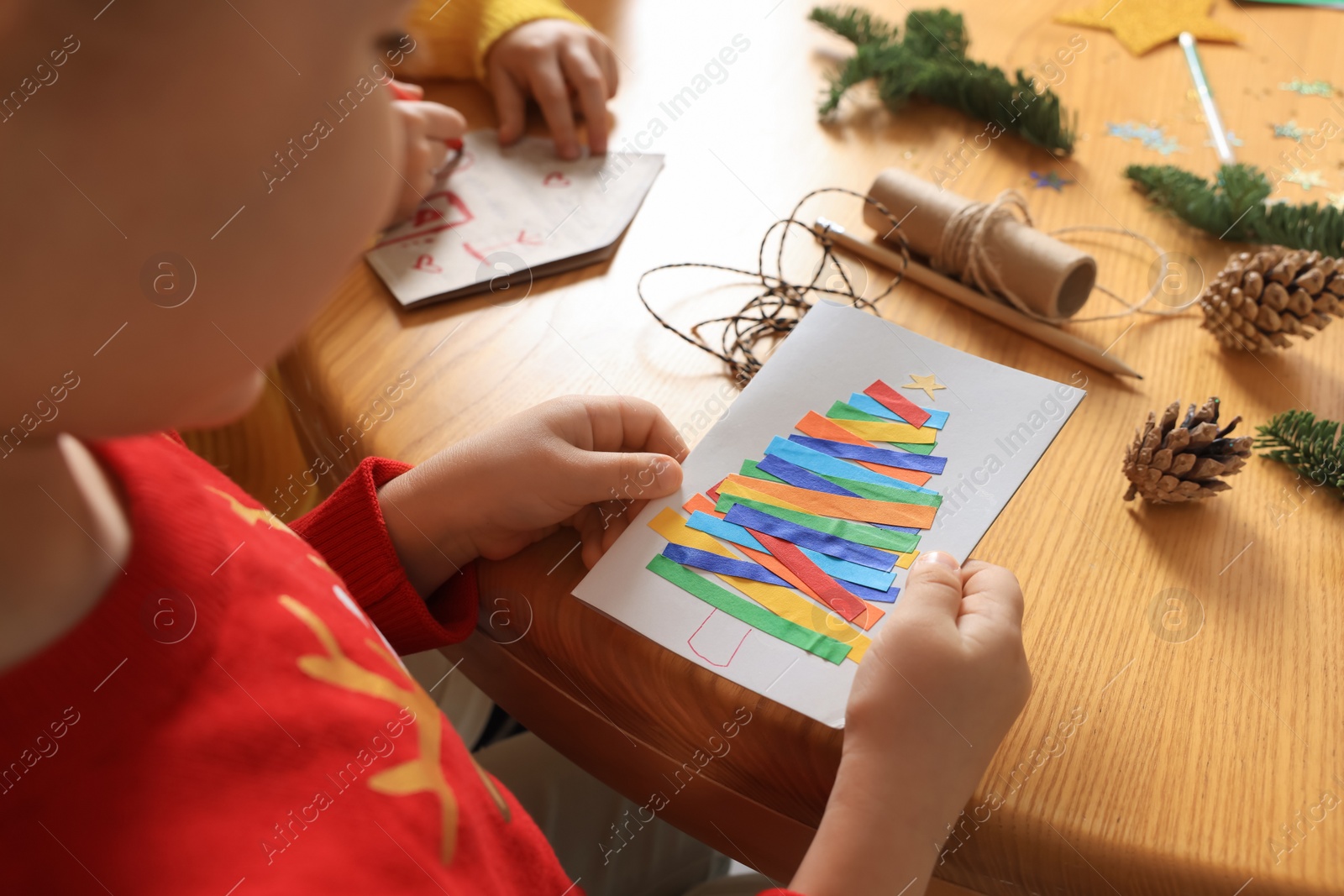 Photo of Little child with beautiful Christmas greeting card at wooden table, closeup