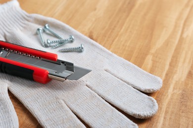 Photo of Utility knife, screws and glove on wooden table, closeup. Space for text