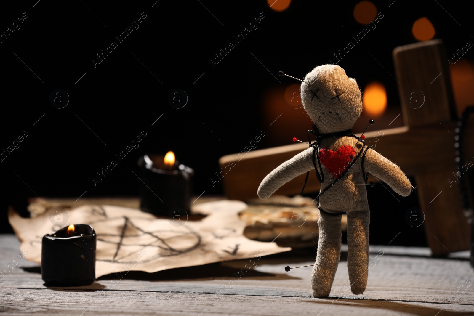 Photo of Voodoo doll pierced with pins and ceremonial items on wooden table against blurred background