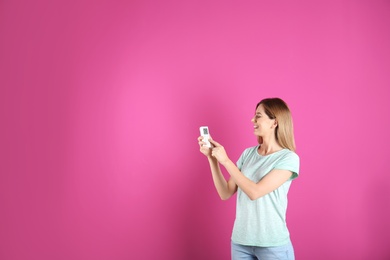 Photo of Woman with air conditioner remote on color background