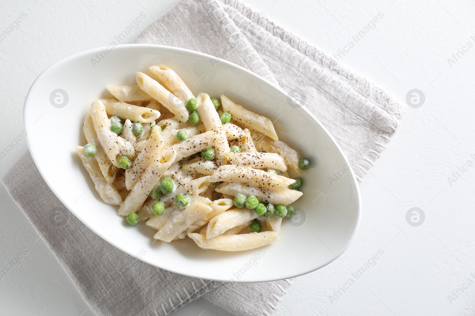 Photo of Delicious pasta with green peas and creamy sauce in bowl on white table, top view