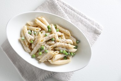 Photo of Delicious pasta with green peas and creamy sauce in bowl on white table, top view