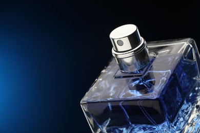 Photo of Luxury men`s perfume in bottle against dark blue background, closeup. Space for text