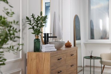 Modern bathroom interior with stylish mirror, eucalyptus branches, vessel sink and wooden vanity