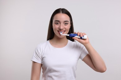 Photo of Happy woman brushing her teeth with electric toothbrush on white background