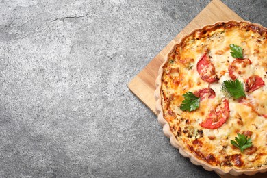 Photo of Tasty quiche with tomatoes, parsley and cheese on grey textured table, top view. Space for text