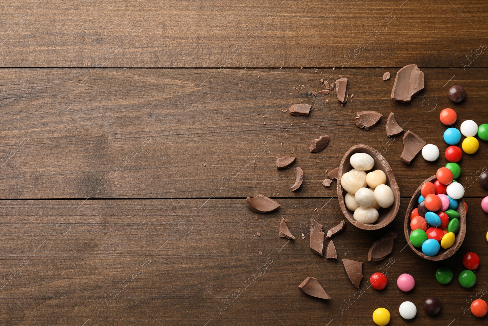 Photo of Broken chocolate egg and colorful candies on wooden table, flat lay. Space for text