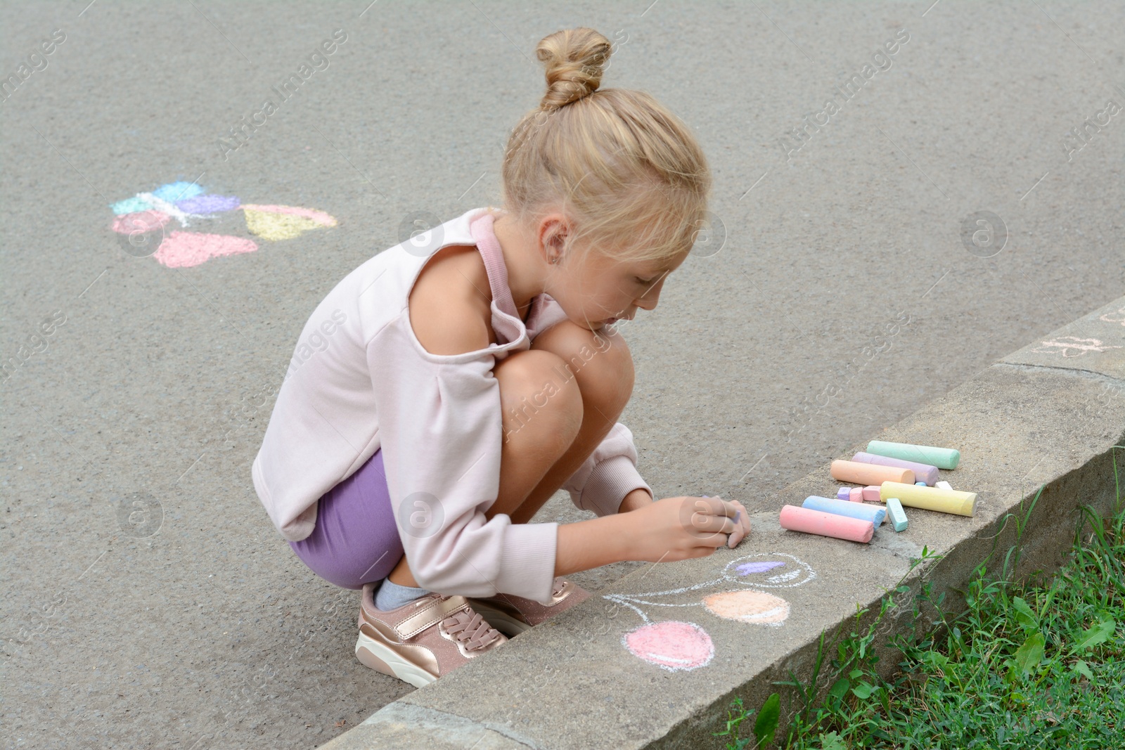 Photo of Little child drawing balloons with chalk on asphalt