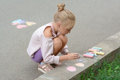 Little child drawing balloons with chalk on asphalt