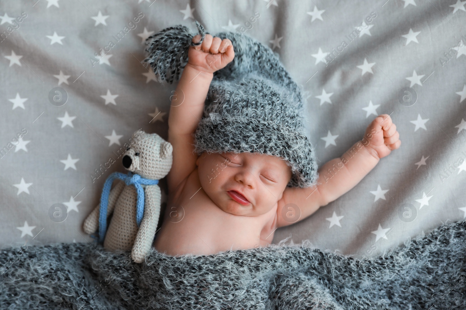 Photo of Cute newborn baby in warm hat with toy sleeping on bed, top view