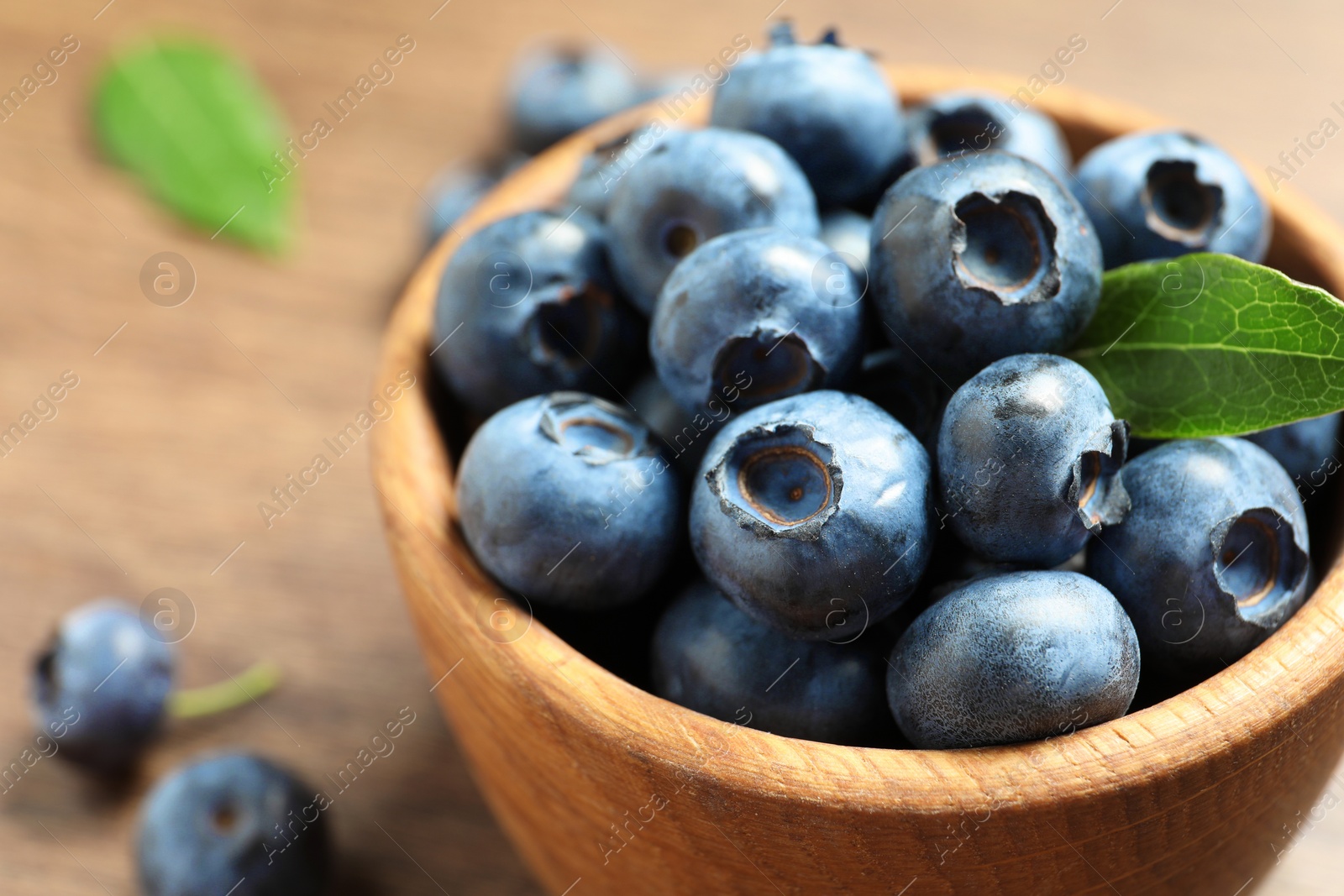 Photo of Bowl of tasty fresh blueberries with green leaves on table, closeup. Space for text